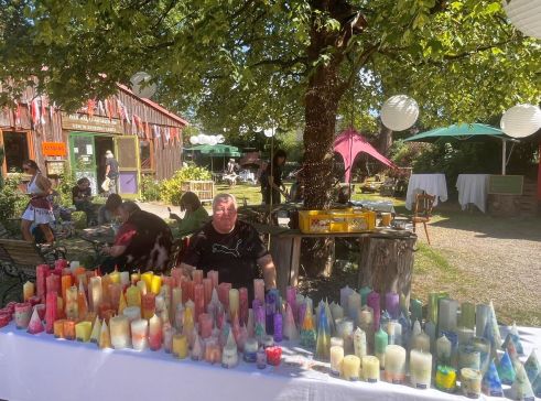Kerzenstand mit vielen bunten Kerzen und Standbetreuer. Im Hintergrund die Flohmarkthalle.